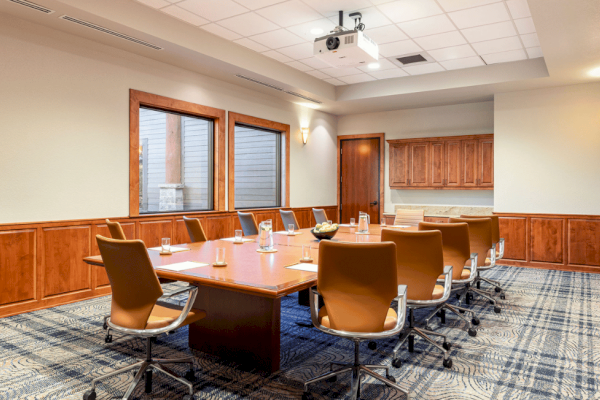 The image shows a conference room with a large table at Riverhouse Lodge in Bend Oregon, nine chairs, a ceiling-mounted projector, windows, and wood-paneled walls.