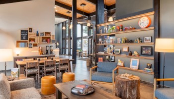 This is a cozy, modern lounge at Riverhouse Lodge in Bend, OR with wooden furniture, colorful decor, and shelves filled with books and knick-knacks.