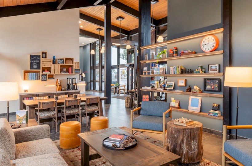 This is a cozy, modern lounge at Riverhouse Lodge in Bend, OR with wooden furniture, colorful decor, and shelves filled with books and knick-knacks.