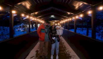 A family walking through a covered, well-lit bridge at night, surrounded by snow.