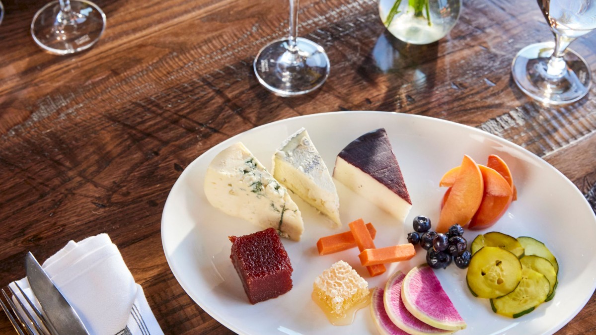 A dining table at Currents Restaurant at Riverhouse Lodge in Bend, Oregon with a cheese and vegetable platter, glasses of champagne, a plate of food, a napkin with cutlery, and a small vase of flowers.