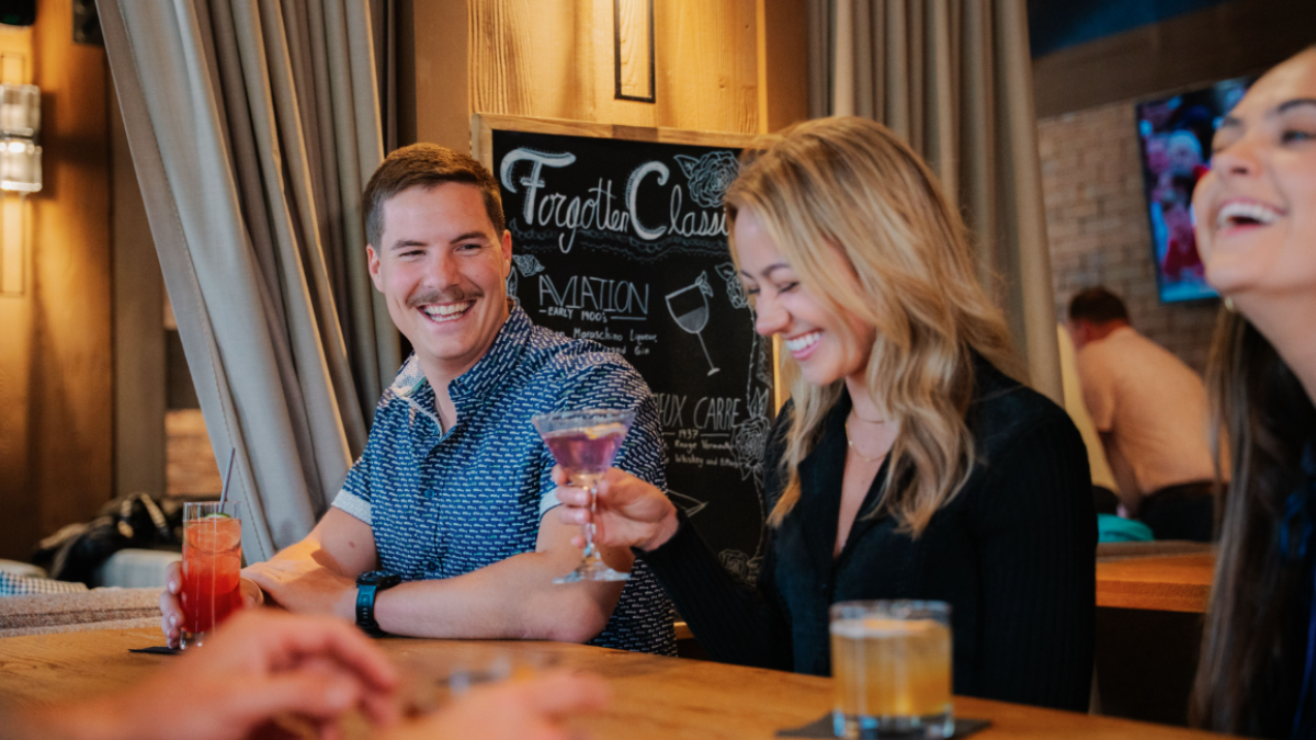 People are laughing and enjoying drinks at Currents at the Riverhouse in Bend, Oregon with a chalkboard menu in the background.