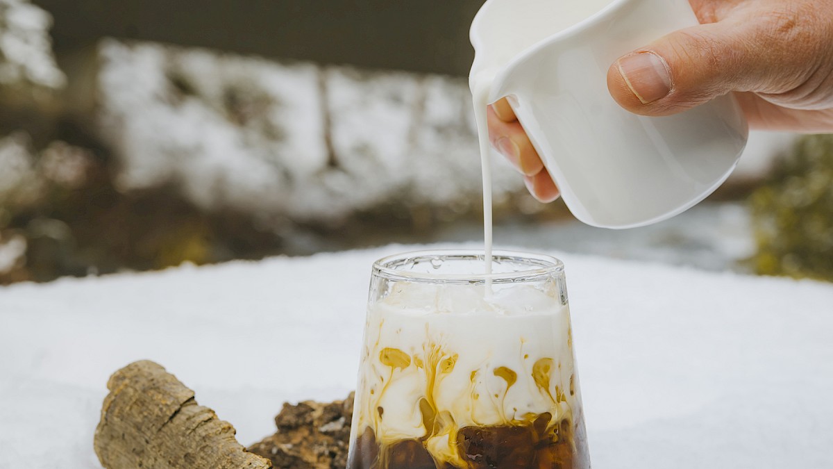 Hand pouring cream into an iced cocktail at Currents at Riverhouse Lodge, home to some of the best cocktails in Bend and Central Oregon, set against a snowy forest backdrop.