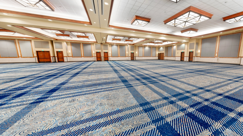 An empty, spacious conference room with patterned blue carpet, high ceiling, and geometric light fixtures.