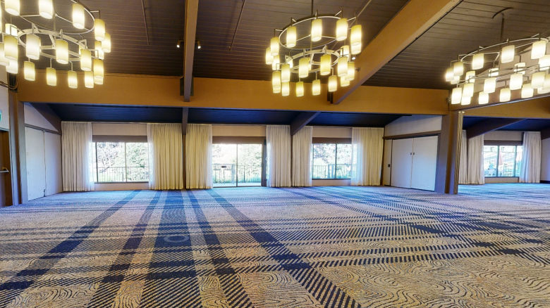 An empty, spacious room with patterned carpet, large windows with curtains, and modern chandeliers hanging from the ceiling.