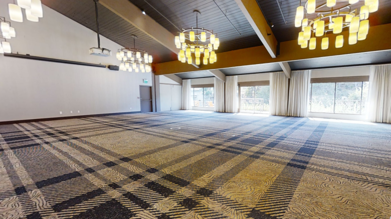 A spacious room with a patterned carpet, large windows, and multiple chandeliers hanging from a wooden ceiling.