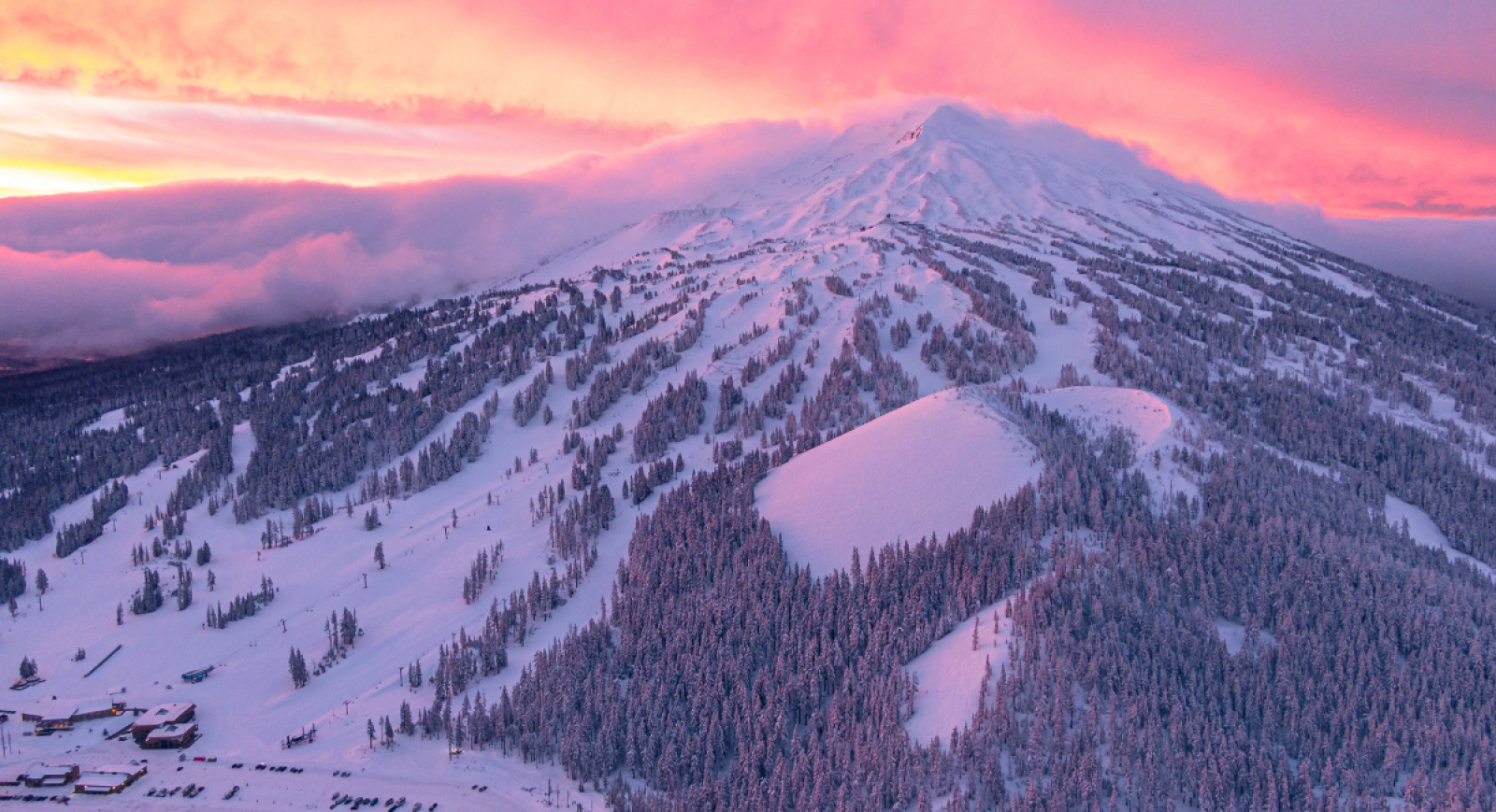 Snow-covered Mt. Bachelor in Central Oregon at sunset, with vibrant pink and orange skies above tree-lined slopes—one of the best skiing destinations in the Pacific Northwest.