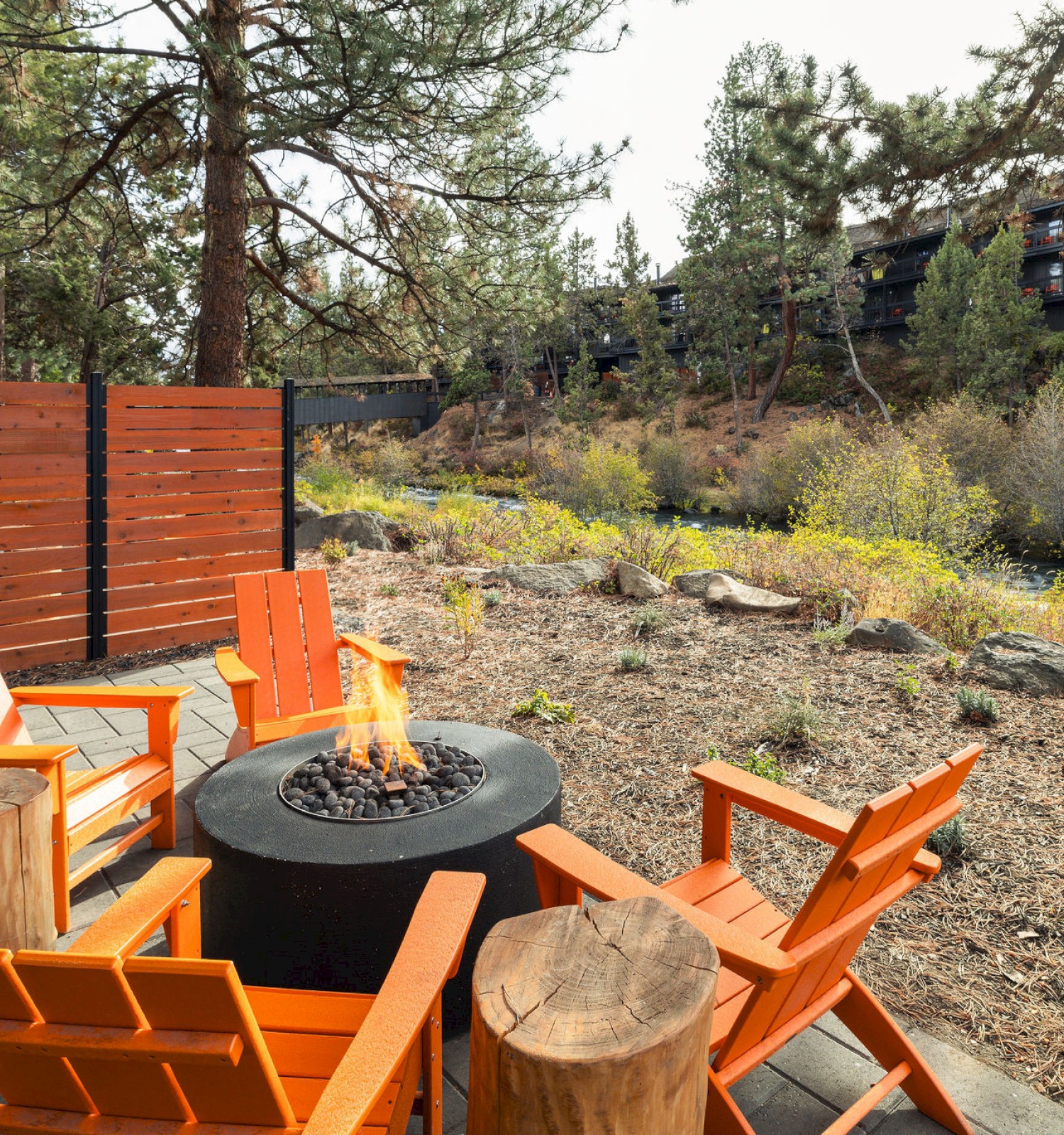 Riverside hotel fire pit seating with orange Adirondack chairs at Riverhouse Lodge in Bend, Oregon—ideal for cozy outdoor stays with Deschutes River views.