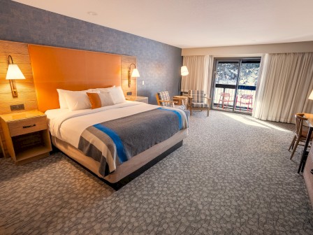 A well-lit modern hotel room at Riverhouse Lodge  with a King bed, side tables, chairs, curtain windows, and a carpeted floor.