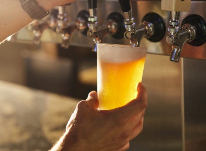 A person is pouring draft beer from a tap into a plastic cup. The tap handles show options like 