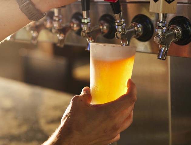 A person is pouring draft beer from a tap into a plastic cup. The tap handles show options like 
