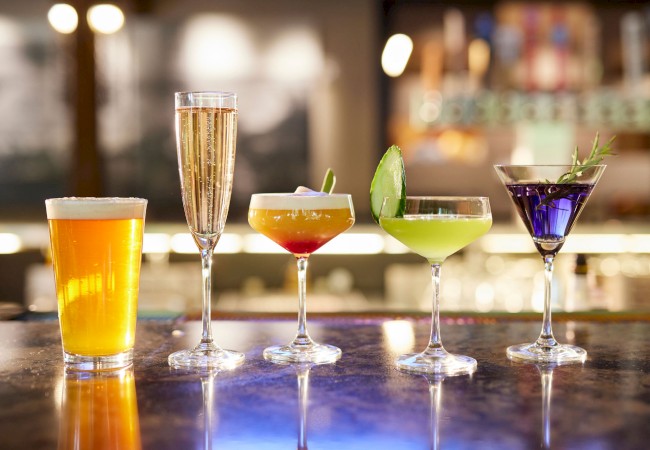 A selection of colorful drinks on a bar counter, including beer, champagne, and cocktails with garnishes in various glasses.