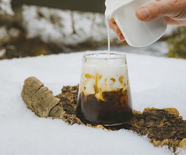 Hand pouring cream into an iced cocktail at Currents at Riverhouse Lodge, home to some of the best cocktails in Bend and Central Oregon, set against a snowy forest backdrop.