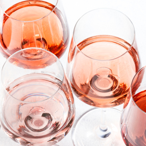 The image shows seven glasses of wine in various shades of red and pink, arranged closely together against a white background.