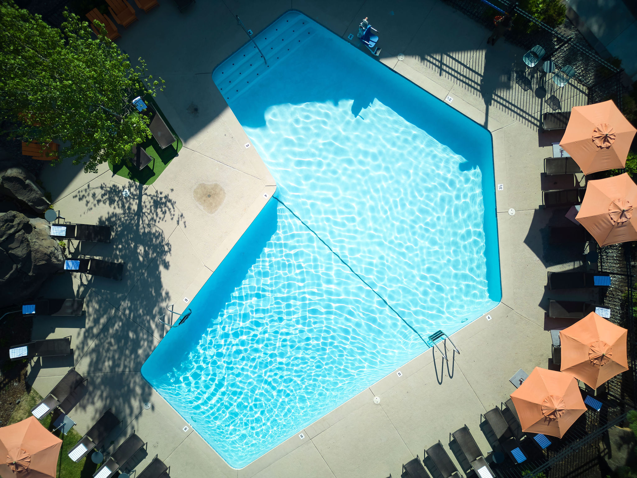 An overhead view of a uniquely shaped swimming pool surrounded by lounge chairs and umbrellas, with a few people relaxing nearby.