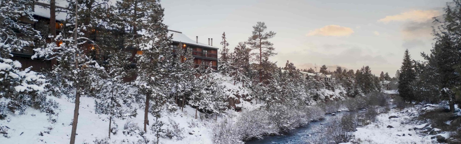 Riverhouse Lodge in Bend Oregon with snowy pine trees and the Deschutes River in winter, perfect hotel stay near Mt. Bachelor for ski trips and winter getaways.