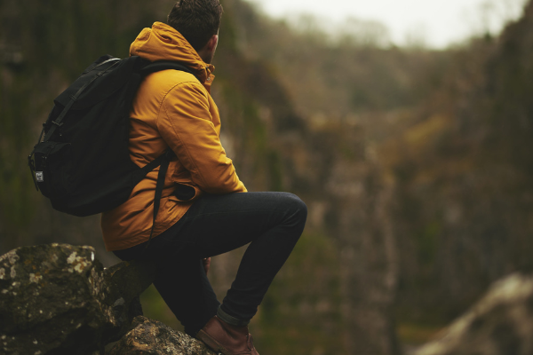 A man with a backpack is sitting on a rock, gazing at a canyon or valley surrounded by trees in Bend Oregon. Riverhouse Lodge is most central hotel in Bend Oregon