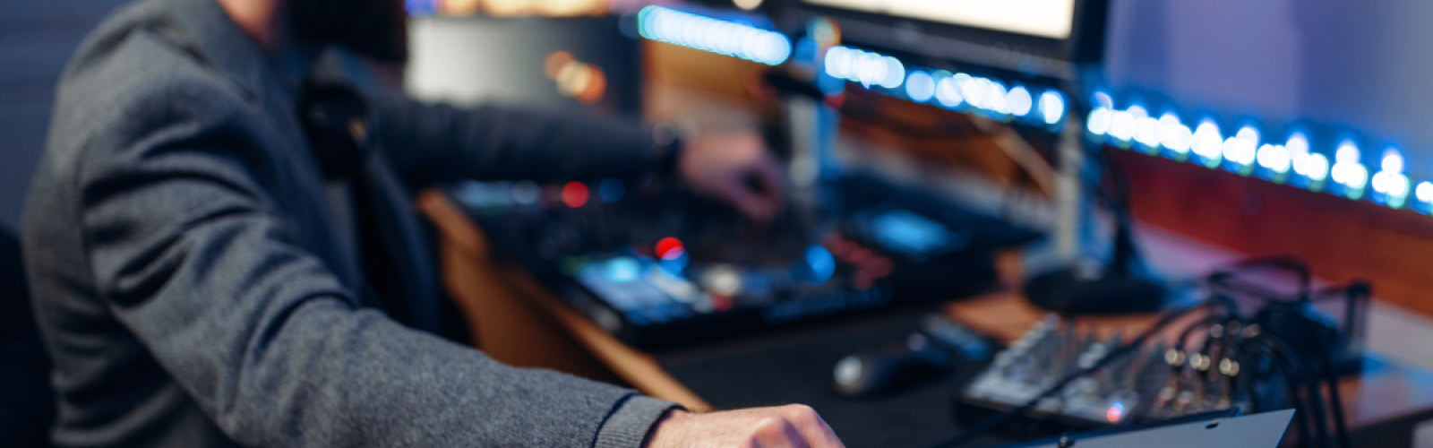 A person operates a sound mixing console in a studio, with multiple screens and audio equipment surrounding them, focused on their work.