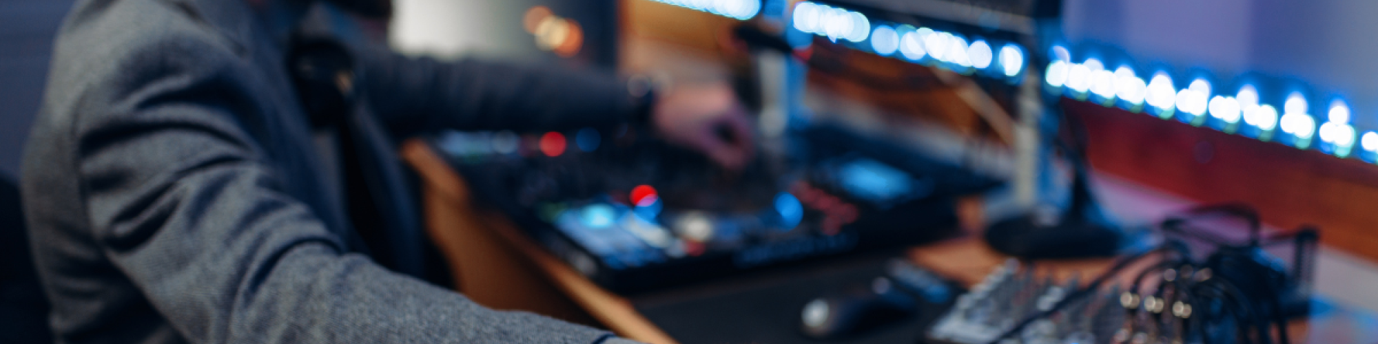 A person operates a sound mixing console in a studio, with multiple screens and audio equipment surrounding them, focused on their work.