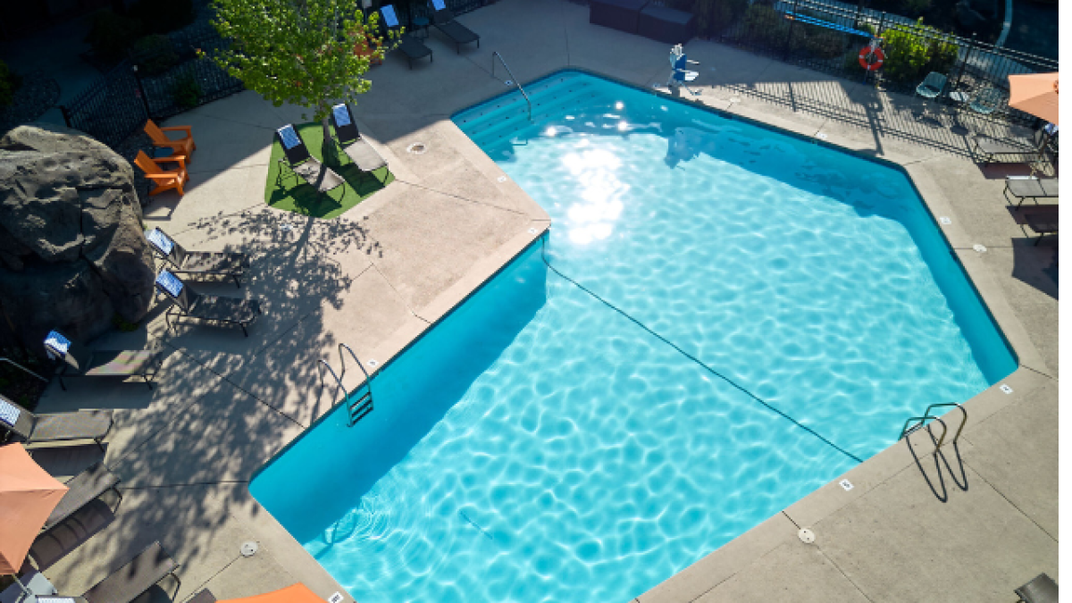 The outdoor swimming pool at Riverhouse Lodge in Bend, Oregon with clear blue water surrounded by lounge chairs and orange umbrellas, situated in a concrete area with some greenery.