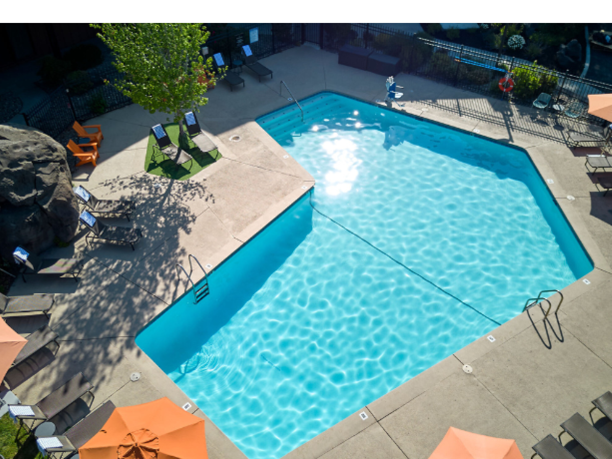 The outdoor swimming pool at Riverhouse Lodge in Bend, Oregon with clear blue water surrounded by lounge chairs and orange umbrellas, situated in a concrete area with some greenery.