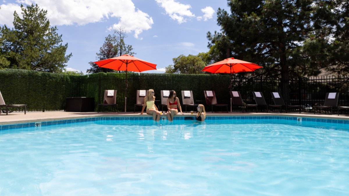 A swimming pool at Riverhouse Lodge in Bend Oregon with lounge chairs, red umbrellas, and people sitting by the poolside on a sunny day.