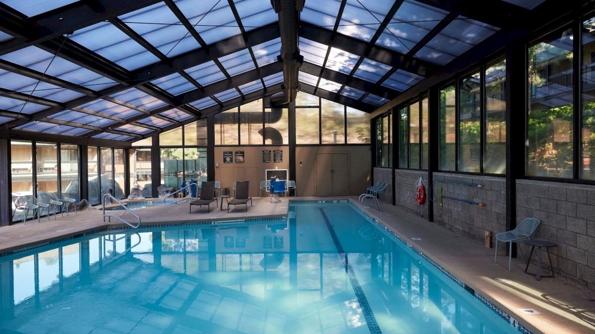 The indoor swimming pool at Riverhouse Lodge located in Bend, Oregon with a glass ceiling, surrounded by lounge chairs and large windows. The environment looks clean and inviting.