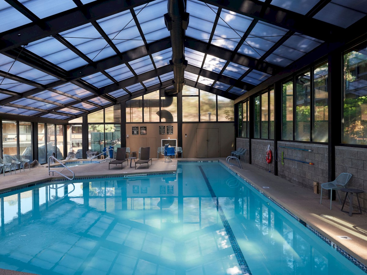 The indoor swimming pool at Riverhouse Lodge located in Bend, Oregon with a glass ceiling, surrounded by lounge chairs and large windows. The environment looks clean and inviting.