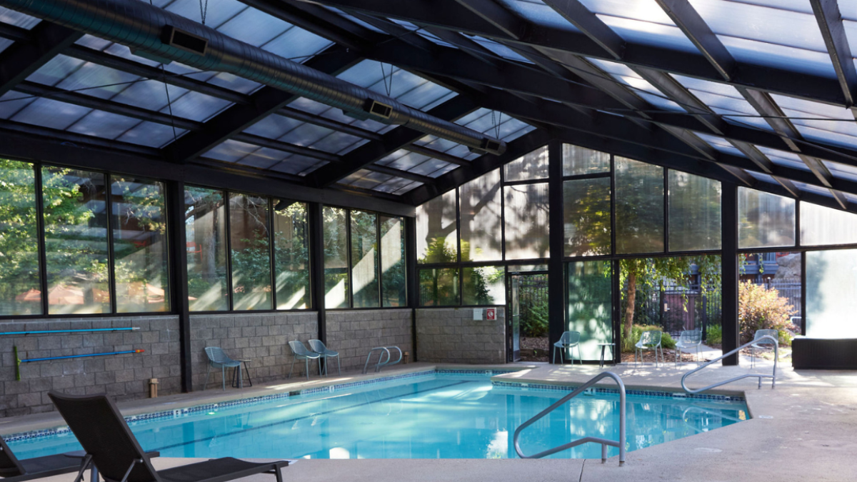 An indoor swimming pool at Riverhouse Lodge in Bend, Oregon with lounge chairs and transparent roof panels allowing natural light to illuminate the space.
