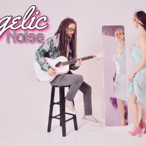 A person with dreadlocks plays guitar on a stool, while a woman in a blue dress and pink heels stands by a mirror. Text reads 