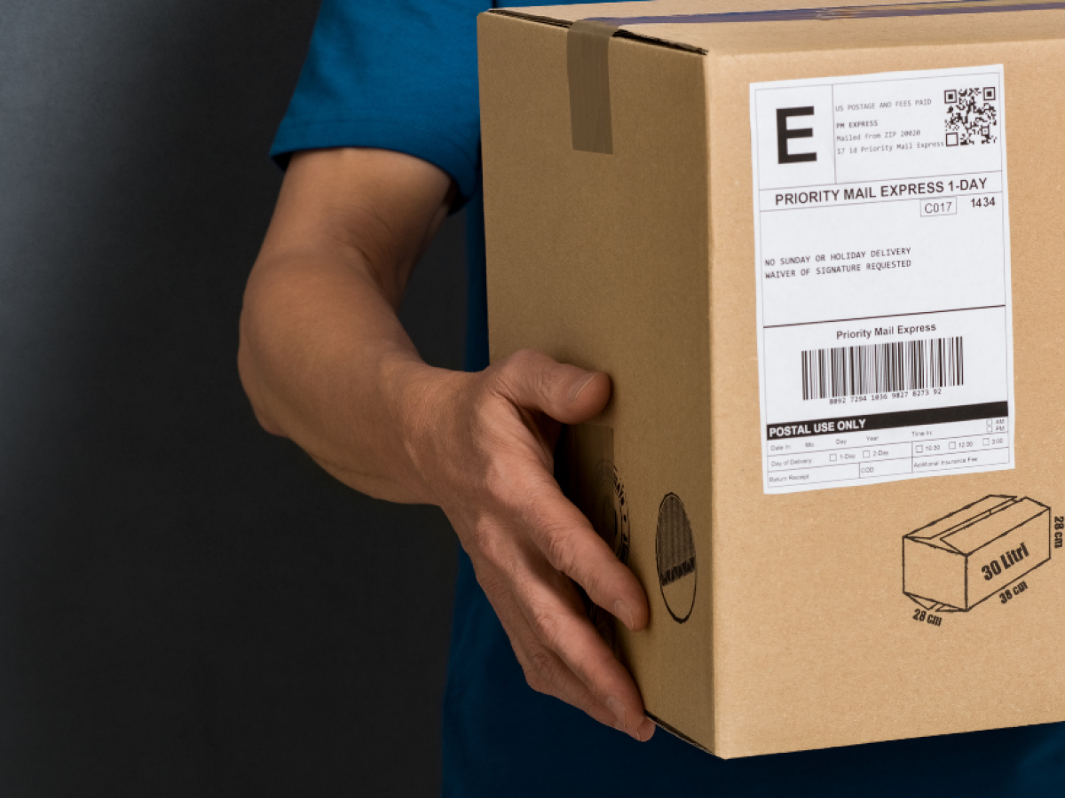 A person is holding a cardboard box with a shipping label and recycling symbol, suggesting it’s ready for delivery.