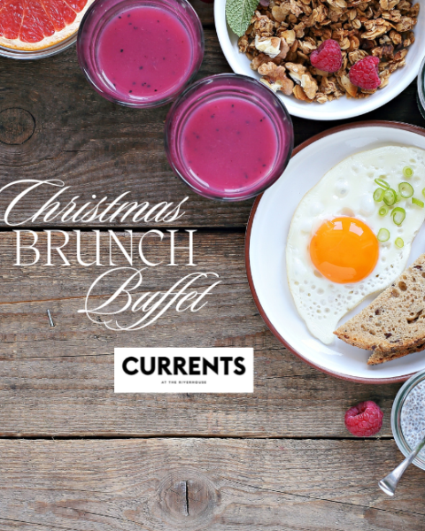 A Christmas brunch buffet with pancakes, berries, juice, granola, salad, bread, and a sunny-side-up egg on a wooden table.