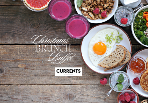 A Christmas brunch buffet with pancakes, berries, juice, granola, salad, bread, and a sunny-side-up egg on a wooden table.