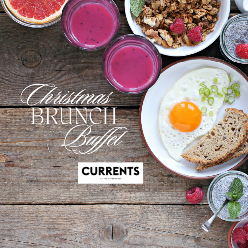 A Christmas brunch buffet with pancakes, berries, juice, granola, salad, bread, and a sunny-side-up egg on a wooden table.