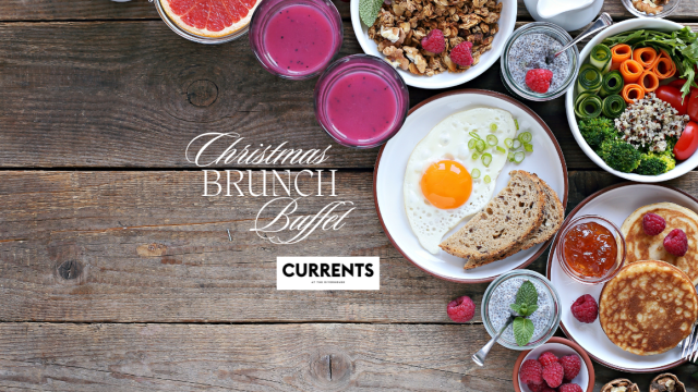 A Christmas brunch buffet with pancakes, berries, juice, granola, salad, bread, and a sunny-side-up egg on a wooden table.