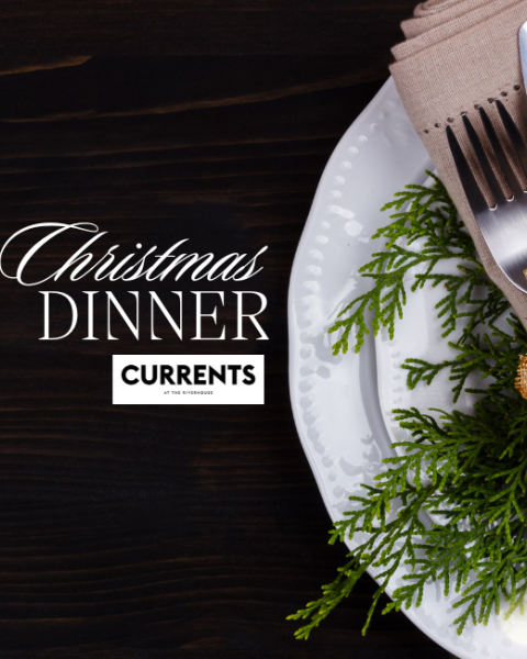 Place setting with a knife and fork wrapped in a napkin, decorated with a gold flower and greenery, on a plate. Text: Christmas Dinner Currents.