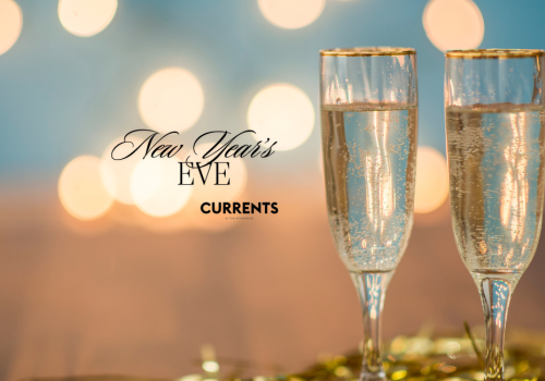 Two champagne flutes with New Year’s Eve text, against a blurred, festive background with bokeh lights.