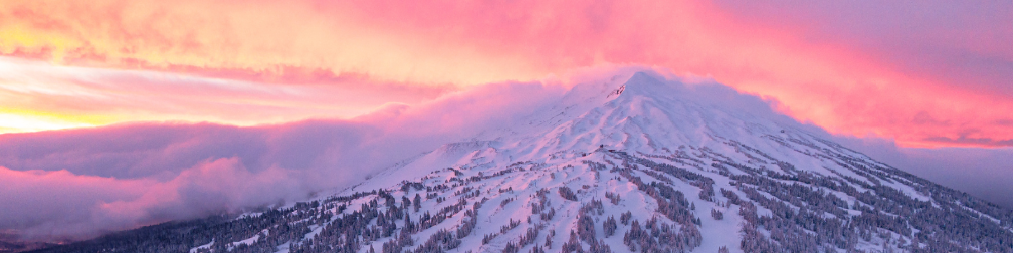 A snow-covered mountain bathed in a vibrant pink sunset, with ski trails and trees visible on its slopes.