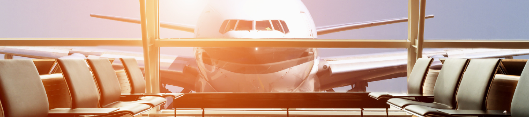 An airplane is seen through the large windows of an empty airport waiting area, with sunlight illuminating the interior.