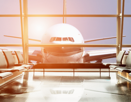 An airplane is seen through the large windows of an empty airport waiting area, with sunlight illuminating the interior.