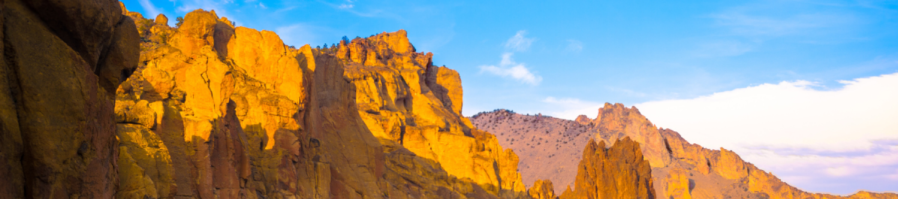 A dramatic landscape with towering orange cliffs illuminated by sunlight, a winding river below, and scattered greenery throughout.