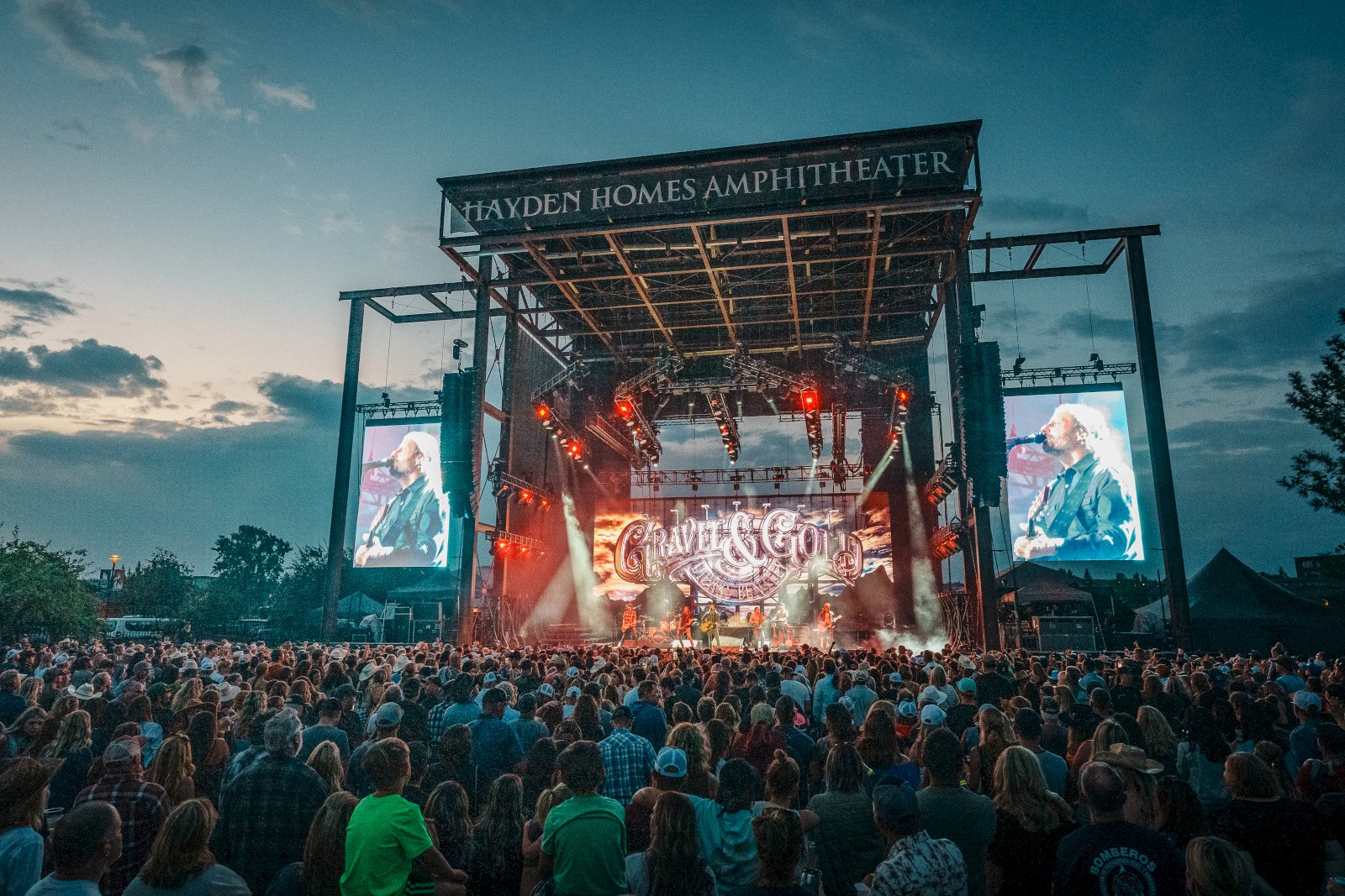 A large crowd enjoys a concert at Hayden Homes Amphitheater, with vibrant stage lighting and big screens displaying the band in Bend Oregon