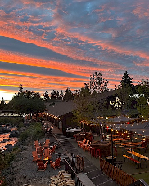 Outdoor dining at Currents restaurant in Bend, Oregon, with riverside seating under string lights at sunset, surrounded by trees along the Deschutes River.