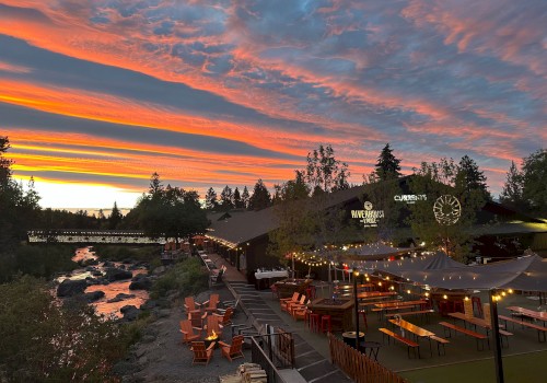 Outdoor dining at Currents restaurant in Bend, Oregon, with riverside seating under string lights at sunset, surrounded by trees along the Deschutes River.