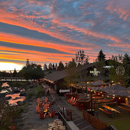 Outdoor dining at Currents restaurant in Bend, Oregon, with riverside seating under string lights at sunset, surrounded by trees along the Deschutes River.