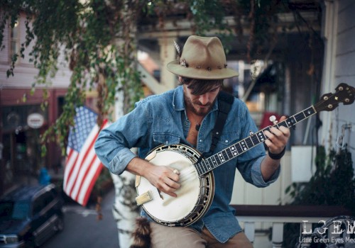 Musician, Oyster Lee, plays banjo on a porch during Father’s Day at Currents at Riverhouse Lodge in Bend, Oregon, with greenery and an American flag in the background.