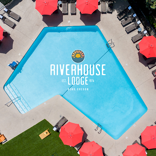 An aerial view of a swimming pool at Riverhouse Lodge, surrounded by red umbrellas, lounge chairs, and a lush green area in Bend, Oregon.