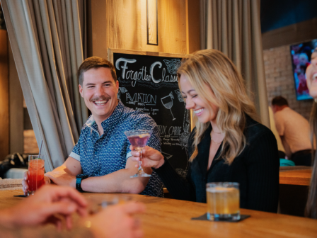 A group of people are sitting at a bar, enjoying drinks in the Lounge of Currents at Riverhouse Lodge in Bend, Oregon and smiling.
