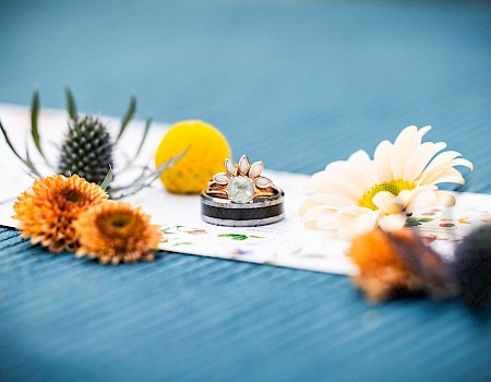 Rings with a floral design are placed on a colorful surface, surrounded by various flowers and natural elements.