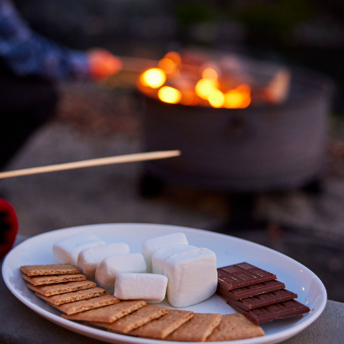 Graham crackers, chocolate, and marshmallows arranged by a cozy fire pit at Riverhouse Lodge—perfect for evening s’mores along the river.